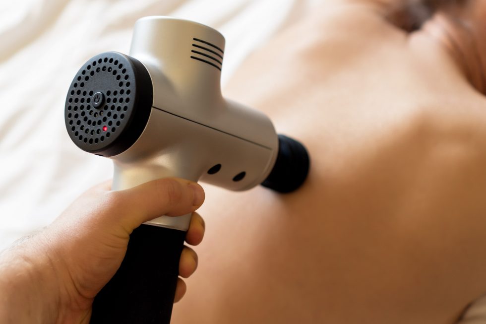 A massage therapist uses a percussion gun on a patient during percussion th...